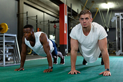 Front view of young handsome diverse male athletics exercising together in fitness center. Bright modern gym with fit healthy people working out and training