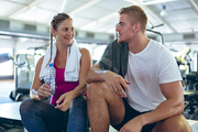 Front view of young Caucasian male and female athlete interacting with each other in fitness center. Bright modern gym with fit healthy people working out and training