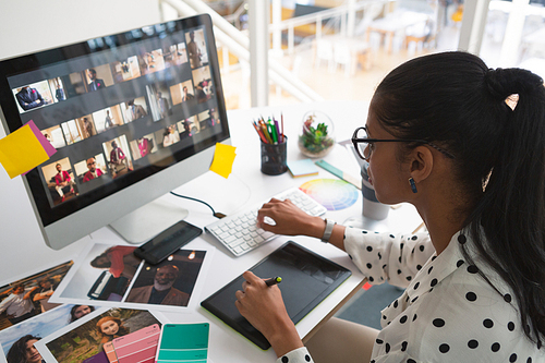 High angle view of young pretty mixed-race female graphic designer working on computer at desk in office. Modern casual creative business concept