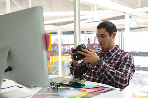 Front view of handsome young Caucasian male graphic designer using digital camera on desk at office. Modern casual creative business concept