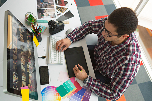 High angle view of handsome young Caucasian male graphic designer working on computer at desk in office. Modern casual creative business concept