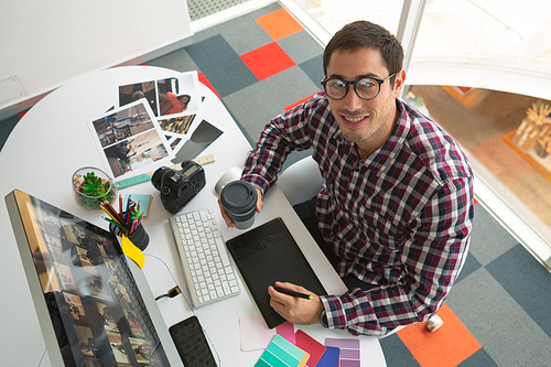 High angle view of handsome Caucasian male graphic designer working on computer at desk in office. Modern casual creative business concept