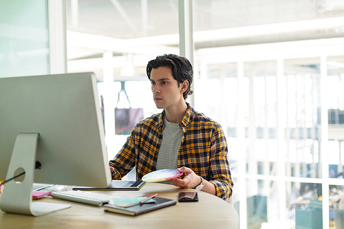 Front view of handsome Caucasian male graphic designer using graphic tablet at desk in office. New start-up business with entrepreneur working hard