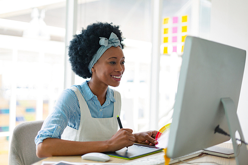 Front view of beautiful mixed-race female graphic designer using graphic tablet at desk in office. New start-up business with entrepreneur working hard