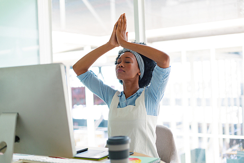 Front view of beautiful young mixed-race female graphic designer performing yoga at desk in office. New start-up business with entrepreneur working hard