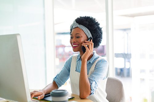 Front view of beautiful mixed-race female graphic designer talking on mobile phone at desk in office. New start-up business with entrepreneur working hard