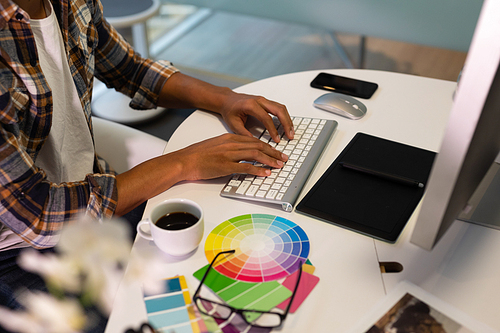 Mid section of mixed race male graphic designer working on computer at desk in office. This is a casual creative start-up business office for a diverse team