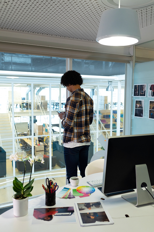 Rear view of young handsome mixed-race male graphic designer using mobile phone in office. This is a casual creative start-up business office for a diverse team