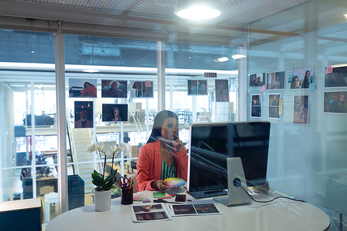 Side view of pretty young Asian female Graphic designer working on computer at desk in office. This is a casual creative start-up business office for a diverse team