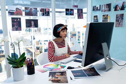 Front view of young pretty Asian female graphic designer using graphic tablet at desk in office. This is a casual creative start-up business office for a diverse team