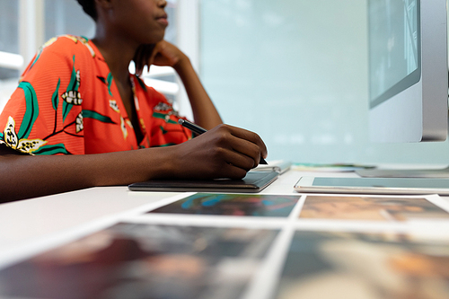 Mid section of African american female graphic designer working on graphic tablet at desk in office. This is a casual creative start-up business office for a diverse team