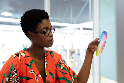 Side view of young African american female graphic designer looking at color swatch in office. This is a casual creative start-up business office for a diverse team