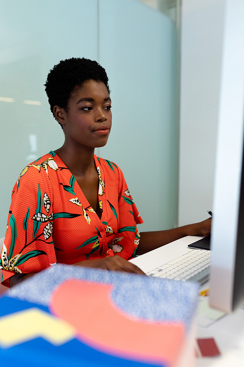 Side view of young pretty African american female graphic designer working on computer at desk in office. This is a casual creative start-up business office for a diverse team