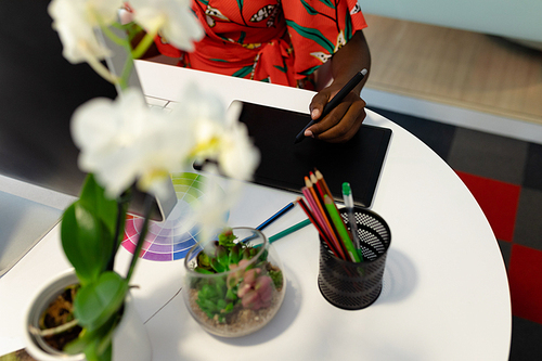 Mid section of African american female graphic designer using graphic tablet at desk. This is a casual creative start-up business office for a diverse team