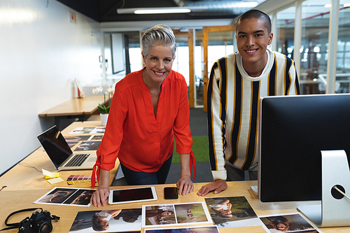 Front view of diverse graphic designers standing together at desk in office. This is a casual creative start-up business office for a diverse team