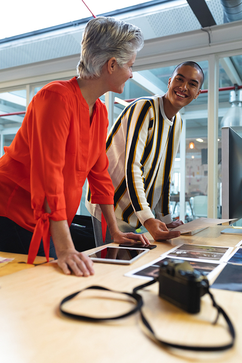 Side view of diverse graphic designers discussing over photographs at desk in office. This is a casual creative start-up business office for a diverse team