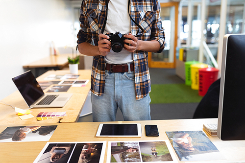 Mid section of handsome mixed-race male graphic designer holding a camera at desk in office. This is a casual creative start-up business office for a diverse team