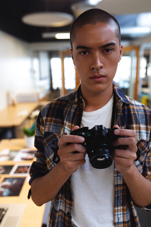 Portrait of mixed race male graphic designer holding a camera in office. This is a casual creative start-up business office for a diverse team