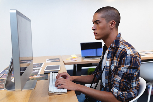 Side view of mixed race male graphic designer working on computer at desk in office. This is a casual creative start-up business office for a diverse team