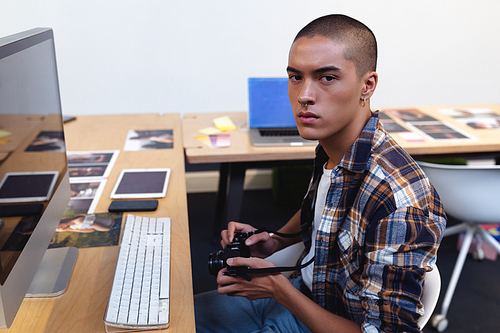 Portrait of mixed race male graphic designer checking a digital camera at desk in office. This is a casual creative start-up business office for a diverse team