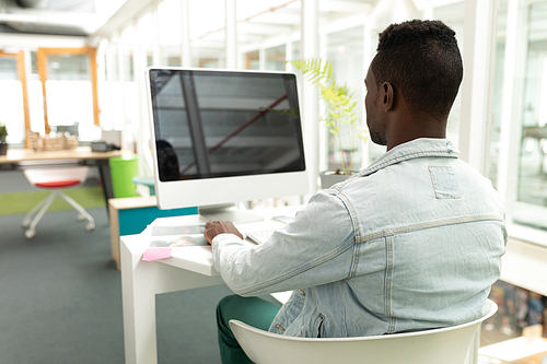 Rear view of African american male graphic designer working on computer at desk in office. This is a casual creative start-up business office for a diverse team