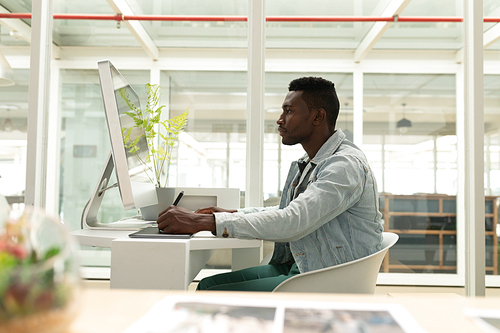 Side view of African american male graphic designer using graphic tablet at desk in office. This is a casual creative start-up business office for a diverse team