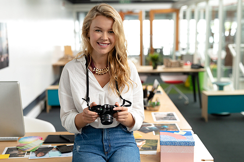 Portrait of Caucasian female graphic designer reviewing photos on digital camera at desk in office. This is a casual creative start-up business office for a diverse team