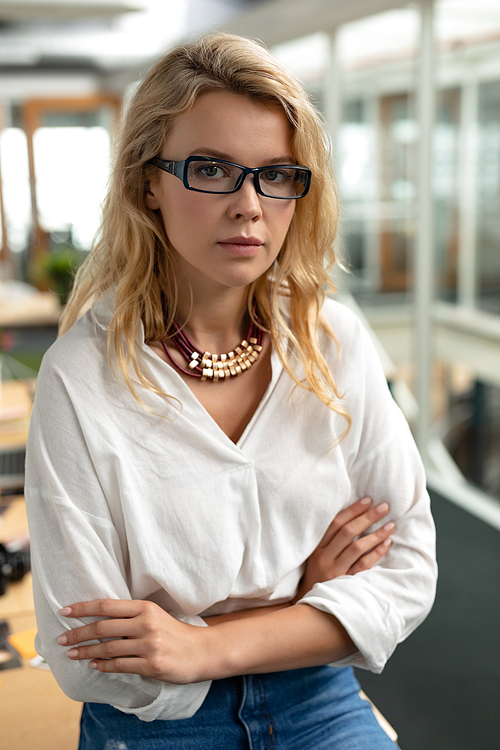 Portrait of Caucasian female graphic designer sitting with arms crossed at desk in office. This is a casual creative start-up business office for a diverse team