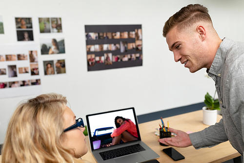 Rear view of Caucasian graphic designers discussing over laptop at desk in office. This is a casual creative start-up business office for a diverse team