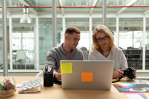 Front view of Caucasian graphic designers discussing over laptop at desk in office. This is a casual creative start-up business office for a diverse team