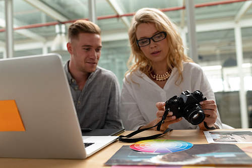 Front view of Caucasian graphic designers discussing over digital camera at desk in office. This is a casual creative start-up business office for a diverse team