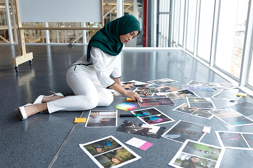 Side view of young mixed race female graphic designer in hijab checking photographs in office. This is a casual creative start-up business office for a diverse team