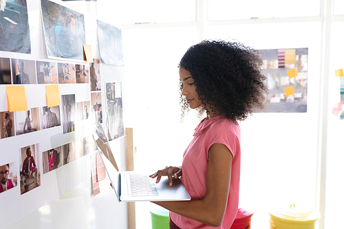 Side view of beautiful African american female graphic designer using laptop in office. This is a casual creative start-up business office for a diverse team