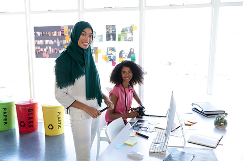 Portrait of diverse female graphic designers smiling at desk in office. This is a casual creative start-up business office for a diverse team