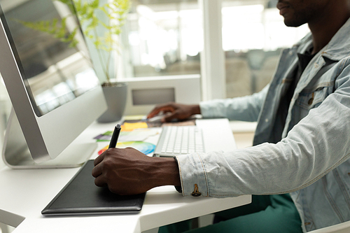 Mid section of African american male graphic designer using graphic tablet at desk. This is a casual creative start-up business office for a diverse team