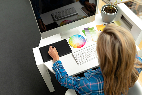 High view of Caucasian female graphic designer using graphic tablet at desk in office. This is a casual creative start-up business office for a diverse team