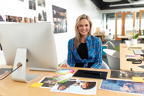 Portrait of happy Caucasian female graphic designer smiling at desk in office. This is a casual creative start-up business office for a diverse team