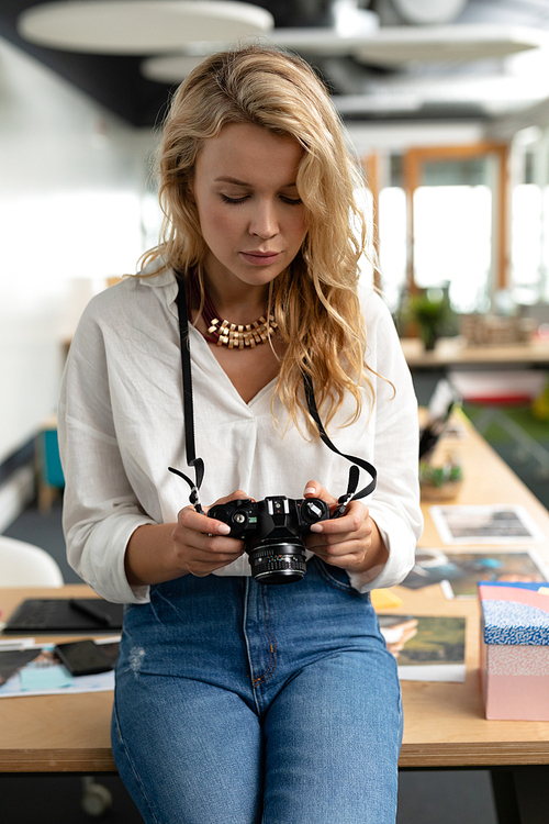 Close-up of Caucasian female graphic designer reviewing photos on digital camera in a modern office. This is a casual creative start-up business office for a diverse team