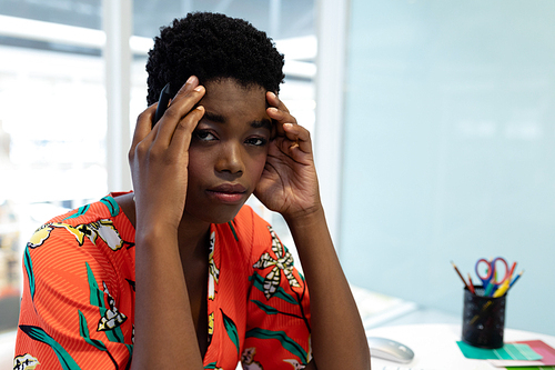 Portrait close up of stressed African american female graphic designer sitting at desk in office. This is a casual creative start-up business office for a diverse team