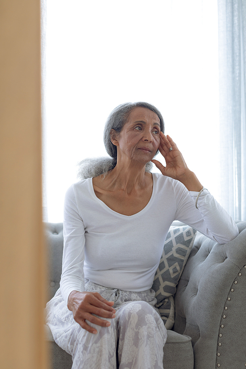 Front view of thoughtful senior mixed race woman sitting on couch at home. Authentic Senior Retired Life Concept