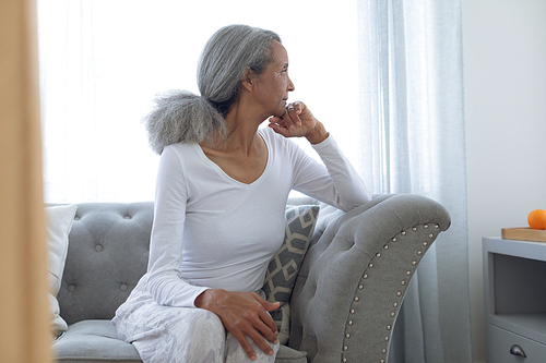 Side view of thoughtful senior mixed race woman sitting on couch at home. Authentic Senior Retired Life Concept