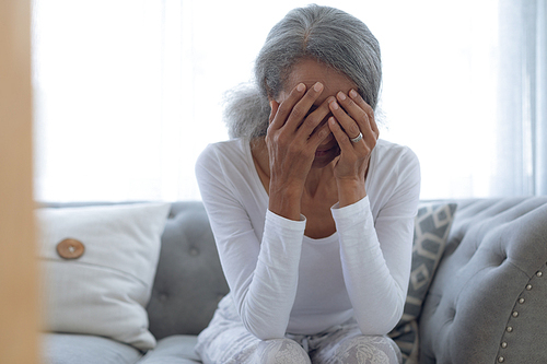 Front view of worried senior mixed race woman sitting on couch at home. Authentic Senior Retired Life Concept