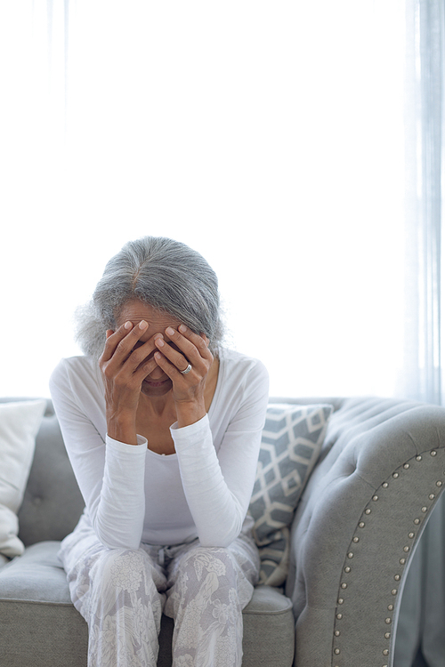 Front view of worried senior mixed race woman sitting on couch at home. Authentic Senior Retired Life Concept