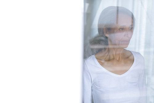 Side view of thoughtful senior mixed race woman standing and looking out the window. Authentic Senior Retired Life Concept