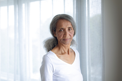 Front view of thoughtful senior mixed race woman standing and looking the camera. Authentic Senior Retired Life Concept