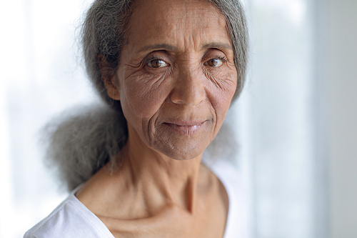 Portrait of thoughtful senior mixed race woman standing inside white room. Authentic Senior Retired Life Concept