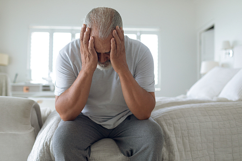 Front view of thoughtful senior Caucasian man sitting on the bed in bedroom. Authentic Senior Retired Life Concept