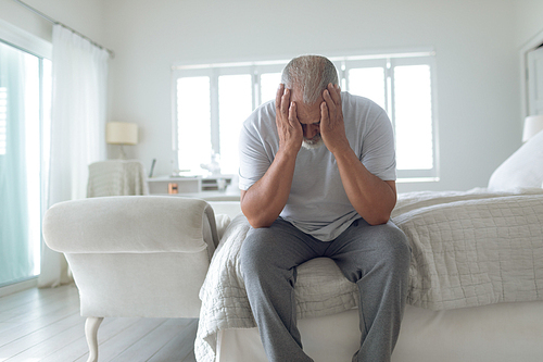 Front view of thoughtful senior Caucasian man sitting on the bed in bedroom. Authentic Senior Retired Life Concept