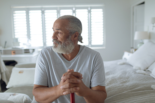 Front view of thoughtful senior Caucasian man sitting on the bed in bedroom. Authentic Senior Retired Life Concept