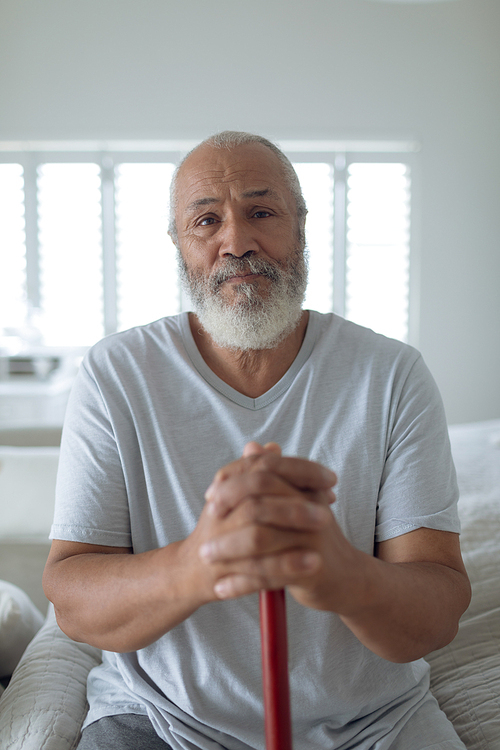 Front view of thoughtful senior Caucasian man sitting on the bed and looking the camera in bedroom. Authentic Senior Retired Life Concept